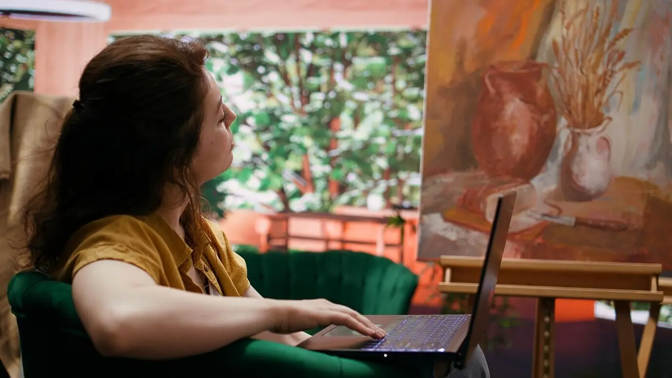 Kadın ressam, kendi sanat ve zanaat atölyesinde çevrimiçi olarak güzel sanatlar için ilham arıyor.