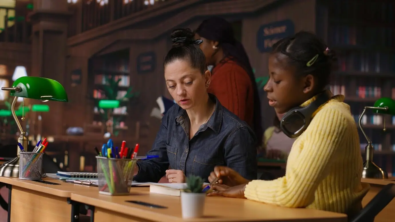 Kütüphane masasında ilkokul çağındaki bir kıza yol gösteren beyaz bir özel öğretmen.